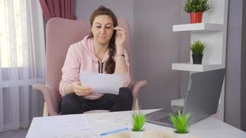 preocupado mujer mirando a ordenador portátil y documentos sensación indefenso. mujer sentado a hogar leyendo malo negativo correos electrónicos y papeleo desesperado. video