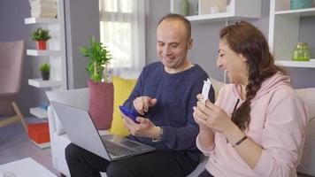 Husband and wife plan the budget. Married couple sitting on sofa at home and reading debit cards and calculating loan debt payments online. video