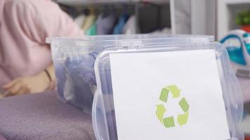 ecológico mulher lança roupas dentro reciclando bin. mulher coloca roupas dentro caixa para reciclando. video