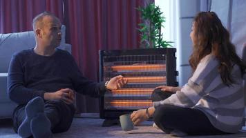 The chilly couple are warming themselves by the electric heater. The cold couple is warming themselves with the electric heater, chatting and sipping their coffee. video