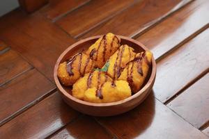 a close up of banana nuggets with chocolate sauce topping served on a wooden bowl. Food concept photo. photo