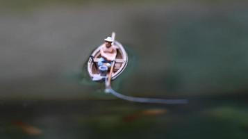 miniatura figura de un pescador pescar en un lago en un pequeño bote. foto