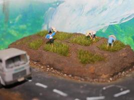 a miniature diorama of a rice field and a road as well as several people and vehicles and buildings. photo