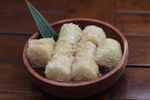 a close up of lupis with grated coconut and brown sugar sauce served in a wooden bowl. Indonesian traditional food photo concept.