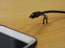 un miniatura figura de un trabajador que lleva un Teléfono móvil cargando cable. foto