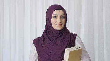 aluna mulher dentro hijab poses para Câmera segurando livros. muçulmano aluna mulher olhando às Câmera e sorridente. video