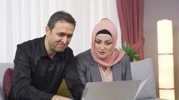 musulmán marido y esposa trabajo a hogar. musulmán Pareja trabajando desde hogar con ordenador portátil.
