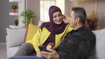 Happy muslim husband and wife spending time at home. Muslim couple looks at the phone at home. video