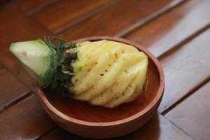 a close up of a peeled pineapple on a wooden bowl. fruit photo concept.