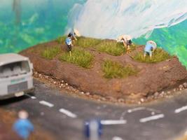 a miniature diorama of a rice field and a road as well as several people and vehicles and buildings. photo