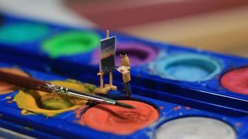 a miniature figure of a painter painting a landscape on watercolors. artist concept. photo