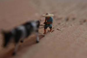 miniatura figura de un granjero arada un campo con su vaca en un cartulina. foto