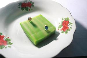 un cerca arriba de un miniatura figura de un granjero quien es agricultura en un verde capa pastel me gusta un arroz campo. granjero agricultura concepto. foto