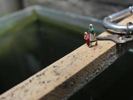 miniatura cifras de madre y niño caminando en un pescado estanque. foto