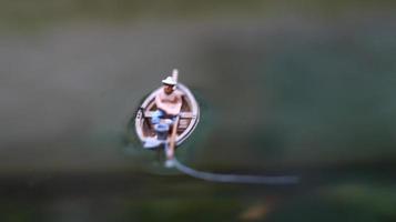 miniatura figura de un pescador pescar en un lago en un pequeño bote. foto