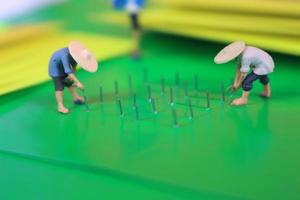 miniature figure of farmers growing crops in the form of staples on green paper. Concept of agriculture photo. photo