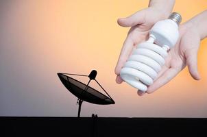 Energy saving concept, Woman hand holding light bulb on satellite dish   background,Ideas light bulb in the hand photo