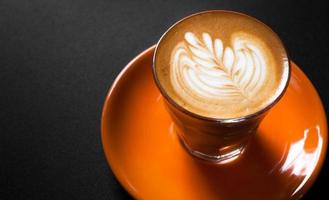 Hot latte in orange cup with floral pattern in foam on a dark background photo