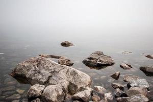 Stones on the lake in the fog. Big and small stones. The water is transparent and under the water you can see stones overgrown with silt. Copy space. photo