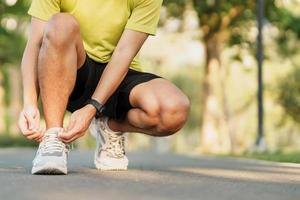 Young athlete man tying running shoes in the park outdoor, male runner ready for jogging on the road outside, asian Fitness walking and exercise on footpath in morning. wellness and sport concepts photo