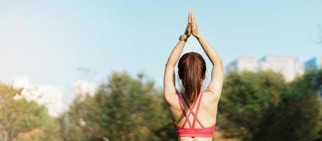 Young adult female in sportswear doing Yoga in the park outdoor, healthy woman sitting on grass and meditation with lotus pose in morning. wellness, fitness, exercise and work life balance concepts photo