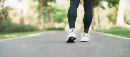 mujer trotar y caminando en el la carretera a mañana, joven adulto hembra en deporte Zapatos corriendo en el parque afuera, pierna músculos de atleta. ejercicio, bienestar, sano estilo de vida y rutina de ejercicio conceptos foto