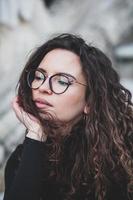 hermosa joven mujer con morena Rizado cabello, retrato en ojo lentes disfrutando el Dom en el ciudad. foto