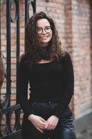 Beautiful young woman with brunette curly hair, portrait in eye glasses enjoying the sun in the city. photo