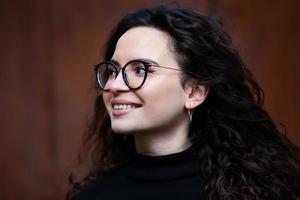 Beautiful young woman with brunette curly hair, portrait in eye glasses enjoying the sun in the city. photo