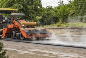 Asphalt paver machine makes a new road and repairing works. A paver finisher, asphalt finisher or paving machine placing a layer of asphalt. Repaving. photo