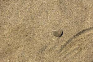 A small stone in the form of heart lies on the sand. photo