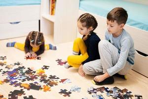 niños conectando piezas de rompecabezas en una habitación para niños en el piso en casa. diversión actividad familiar ocio. foto