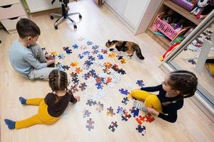 niños conectando piezas de rompecabezas en una habitación para niños en el piso en casa. diversión actividad familiar ocio. foto