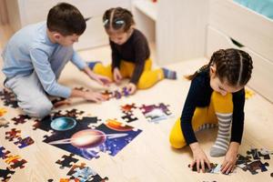 niños conectando piezas de rompecabezas en una habitación para niños en el piso en casa. diversión actividad familiar ocio. foto