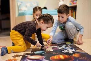 niños conectando piezas de rompecabezas en una habitación para niños en el piso en casa. diversión actividad familiar ocio. foto