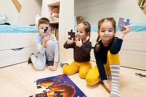 niños conectando piezas de rompecabezas en una habitación para niños en el piso en casa. diversión actividad familiar ocio. foto