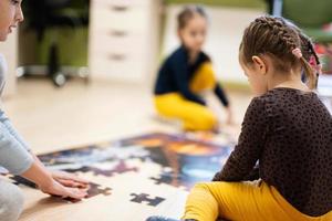 niños conectando piezas de rompecabezas en una habitación para niños en el piso en casa. diversión actividad familiar ocio. foto