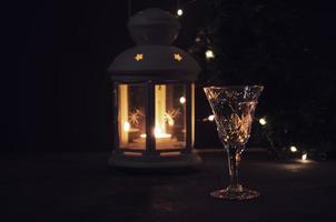 vaso con blanco vino con guirnalda luces y vela linterna en el antecedentes. oscuro fotografía. ardiente vela. dorado bebida en el vaso. hermosa luces reflejado en el vaso. foto