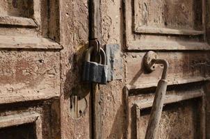 The lock on the old wooden door closeup. Rust on the metal lock. Peeling brown paint on the old door. Ancient texture. photo