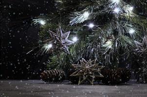 Silver snowflakes, pines and lighting garland on the spruce branch. Falling snow. Christmas still life in vintage style. Gray, black and silver colors. photo