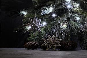 Silver snowflakes, pines and lighting garland on the spruce branch. Christmas still life in vintage style. Gray, black and silver colors. photo