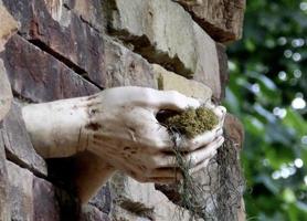 Stone hands in wall holding moss photo