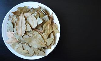 foto un blanco plato con bahía hojas en un oscuro de madera fondo, especias y condimentos, seco plantas