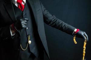 Portrait of Elegant Gentleman in Black Suit and Leather Gloves Leaning on Umbrella on Black Background. Vintage Style and Retro Fashion. photo