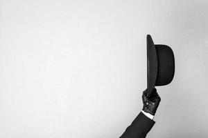 imagen aislada de un caballero con traje oscuro y guantes de cuero quitándose cortésmente el sombrero de bombín. mayordomo británico clásico o empresario británico. foto