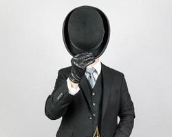 Portrait of English Gentleman in Dark Suit and Leather Gloves Tipping Bowler Hat in Greeting. Classic British Butler or Businessman. photo