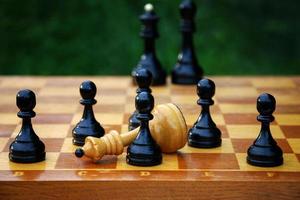 ajedrez final juego - derrotado blanco ajedrez reina rodeado por negro peones foto