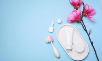 White plastic tubes and jars of cream, and a massage brush for facial cleansing on a blue background, items for cosmetic procedures photo