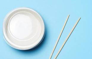 Open empty noodle bowl with and pair of wooden sticks on blue background, top view photo