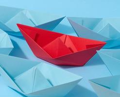 A red paper boat stands in front of a group of blue paper boats, a confrontation photo